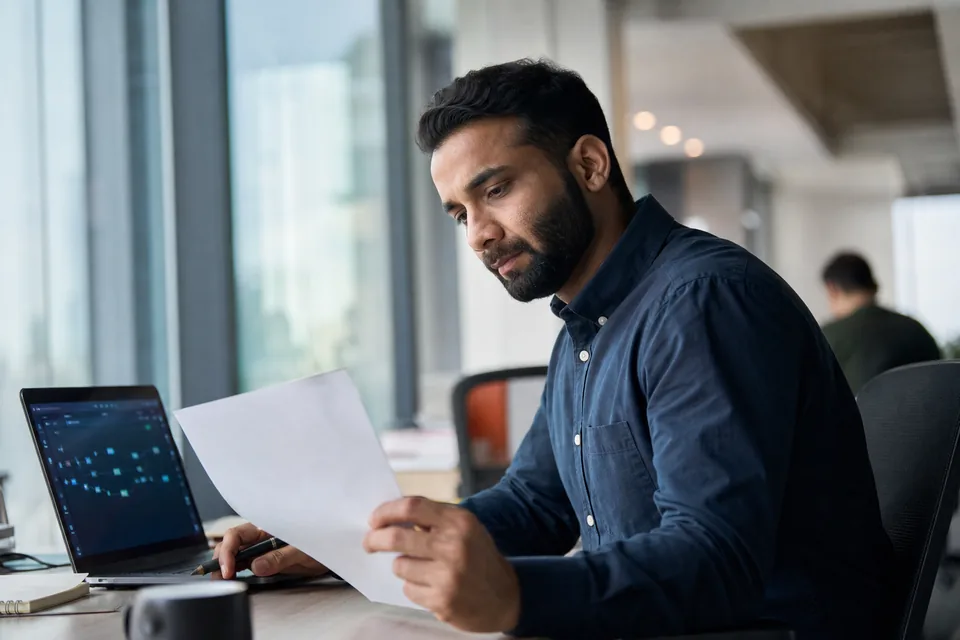 Data platform lead reviewing an enterprise software contract beside a laptop with a pipeline dashboard